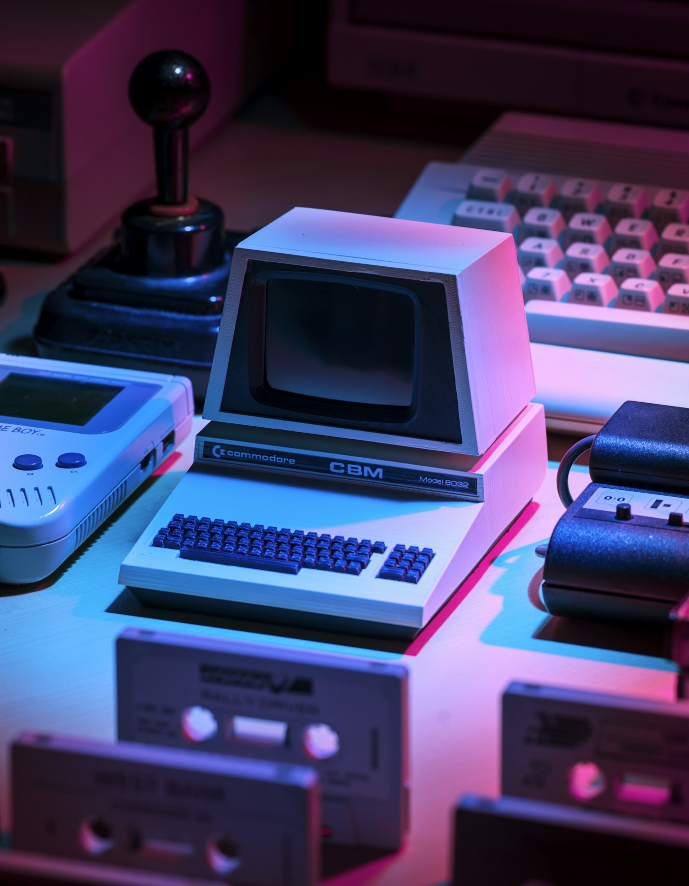 A vintage Commodore computer on a desk with a joystick, Game Boy, and cassette tapes